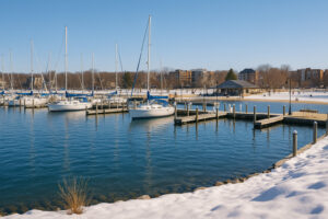 Snowy winter morning at Clinch Park Marina in Traverse City, Michigan, with sailboats docked along the calm blue water.