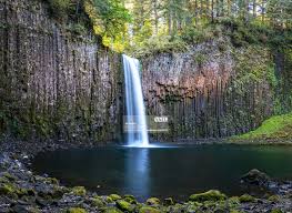 A dramatic waterfall plunging into a prismatic pool within a mossy basalt amphitheater, hidden in Oregon’s secluded Santiam Forest