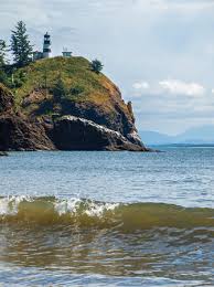 Secluded coves beneath rugged cliffs near a historic lighthouse, where waves crash against jagged rocks and fog blankets the Columbia River mouth.