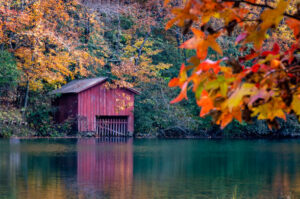 Hidden gems in Alabama: A rustic red boathouse on a calm lake in Mentone, surrounded by vibrant autumn foliage.