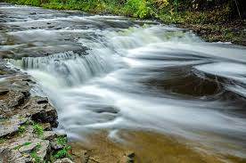 Michigan’s largest Lower Peninsula waterfall, cascading over limestone ledges in a serene state park, blending natural and sculpted rock formations