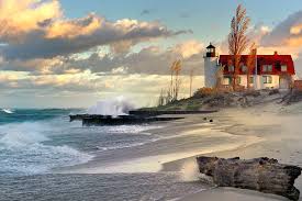 Historic red-roofed lighthouse overlooking a sandy Lake Michigan shore with golden sunset reflections