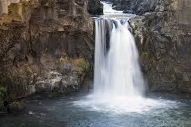 A historic two-tiered waterfall with remnants of an early 1900s power plant, cascading over basalt cliffs into a serene desert canyon.