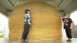 A colossal, densely packed sphere of sisal twine, displayed on a wooden platform in rural Kansas, with a sign noting its growing size from community contributions.