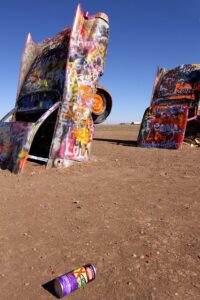 Ten graffiti-covered Cadillacs buried nose-down in a Texas desert field, surrounded by spray-paint cans under a vast sky