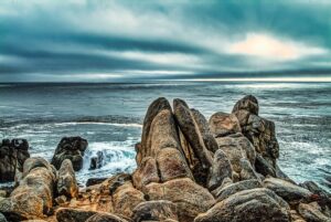 Secluded cove with golden sands, jagged sea stacks, and crashing Pacific waves framed by coastal wildflowers.