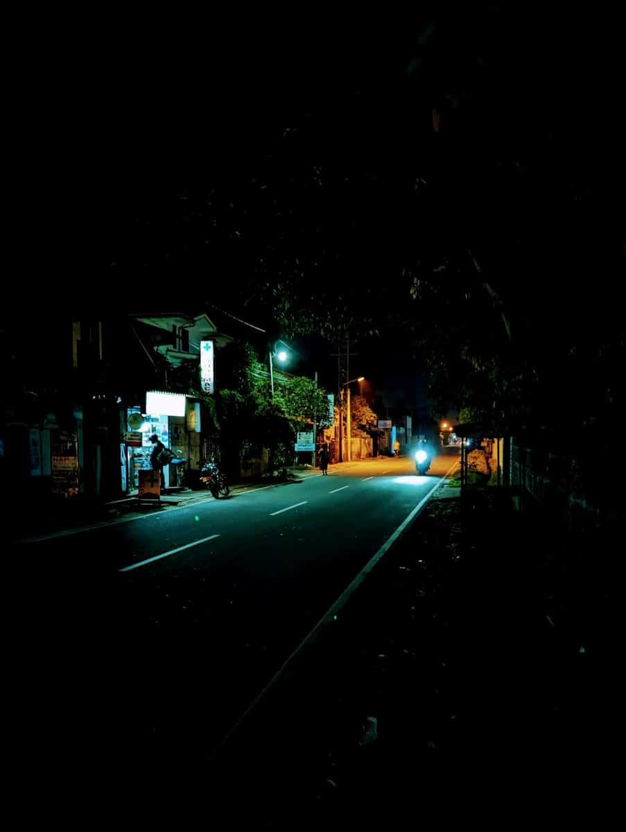A dark street at night with a car driving down it