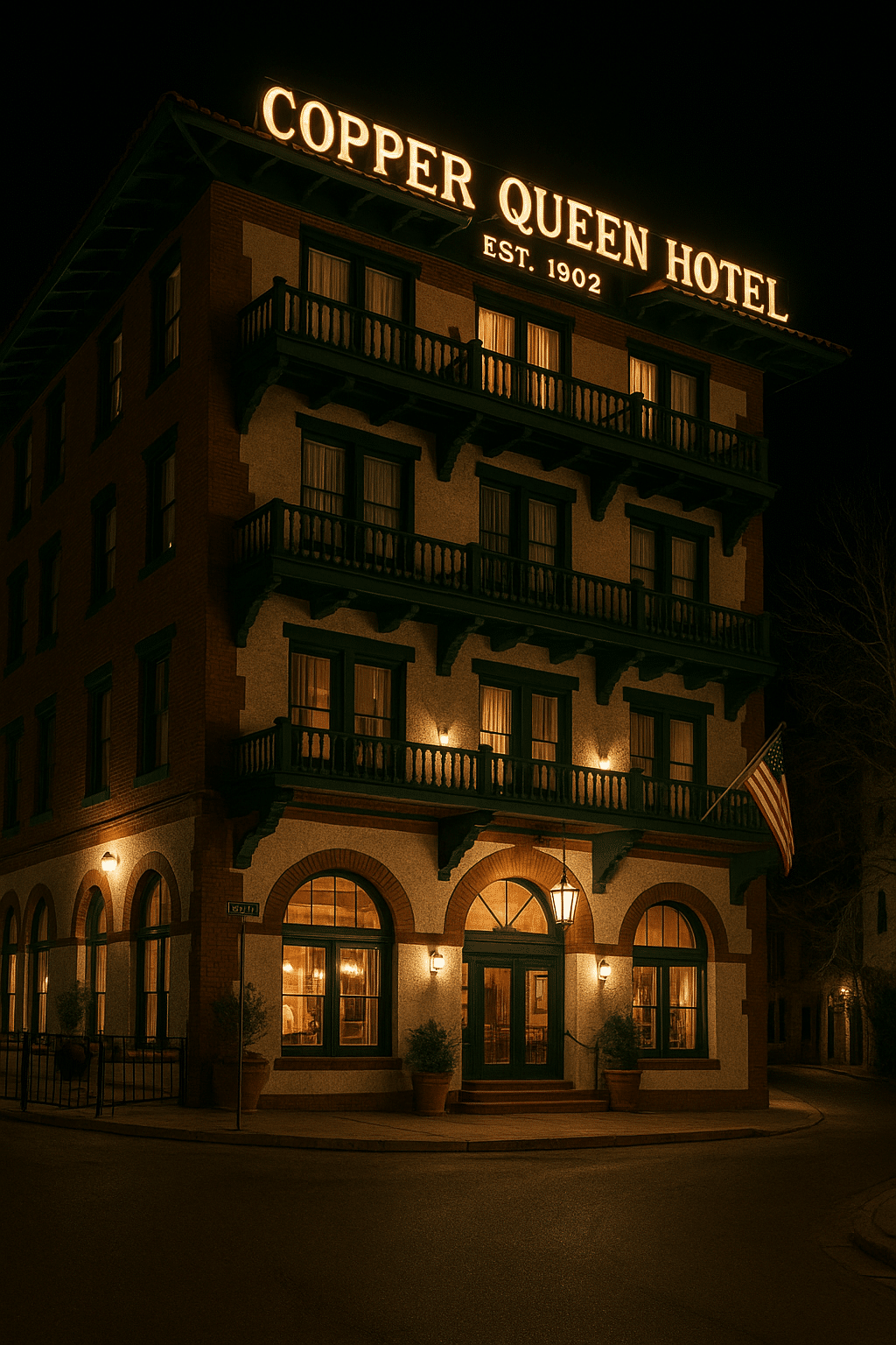 Night view of the historic Copper Queen Hotel in Bisbee, Arizona with glowing windows, red-brick façade, and vintage balconies under a dark sky.